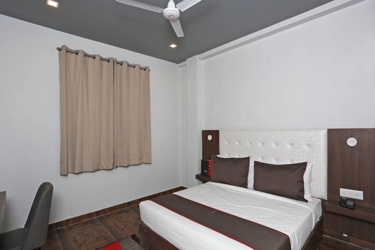 Habitación de hotel con cama, escritorio, silla, ventilador de techo y ventana con cortinas.
