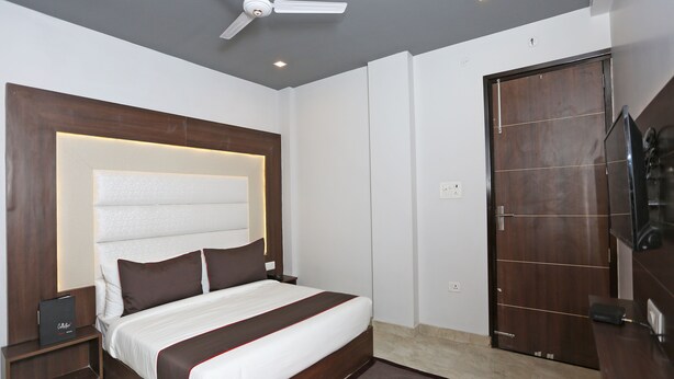 A modern hotel room with a large bed, a ceiling fan, a wooden wardrobe, and a television. - Hotel Arhaan Palace By GRB (New Delhi)