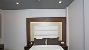 A hotel room with a large bed, a wooden headboard, two bedside tables, and a nightstand with a telephone. - Hotel Arhaan Palace By GRB (New Delhi)