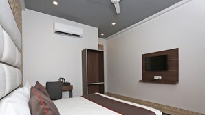A hotel room with a bed, a desk, an air conditioner, a TV, and a wardrobe. - Hotel Arhaan Palace By GRB (New Delhi)