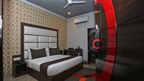 A modern hotel room with a large bed, a ceiling fan, an air conditioning unit, and a red door handle. - Hotel Arhaan Palace By GRB (New Delhi)