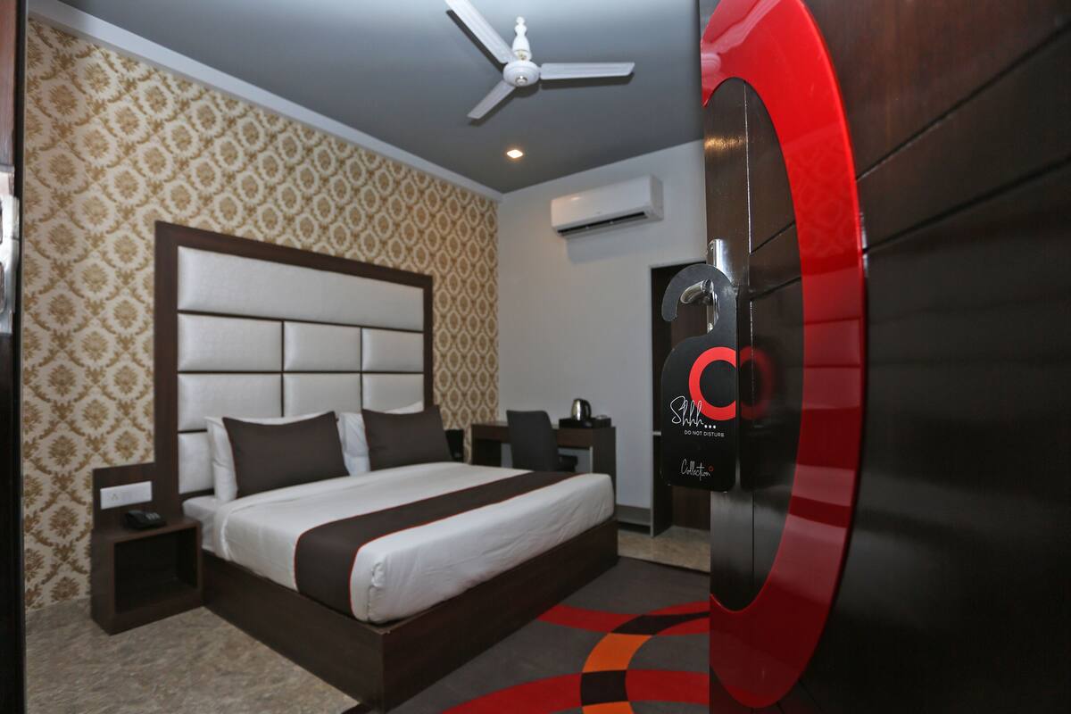 Una habitación de hotel moderna con una cama grande, un ventilador de techo, un equipo de aire acondicionado y un picaporte rojo.