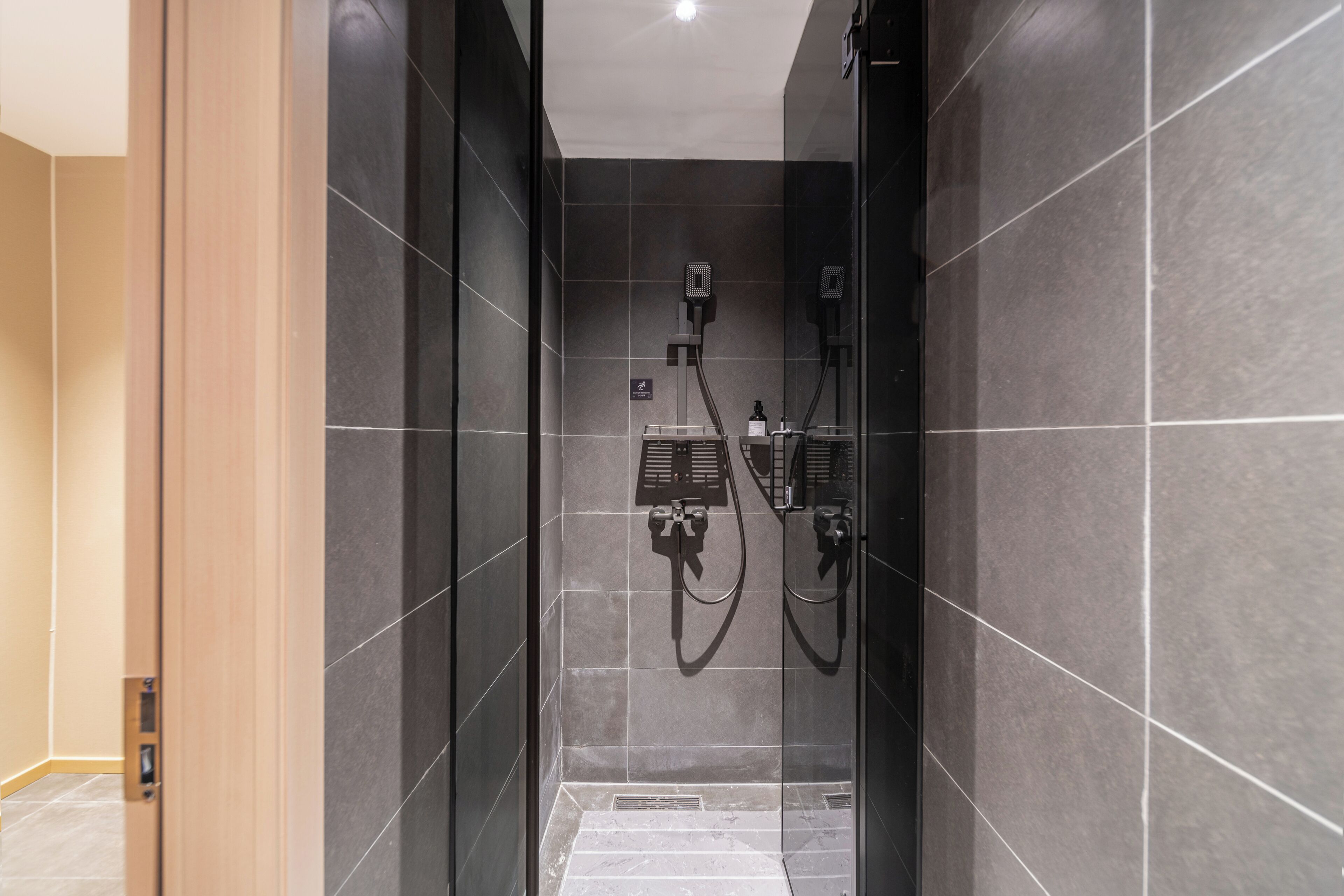 Un baño moderno con paredes de azulejos oscuros, zona de ducha y panel de control visible.