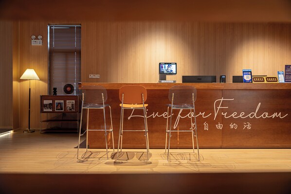 A reception area with a wooden counter, three bar stools, a desk with a computer, and a lamp. - CaptainNo 5YouthHotel XianxiaRoad Branch (Shanghai)