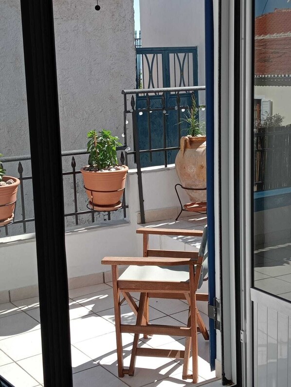 A balcony with terracotta planters, a wooden table, and a blue gate.