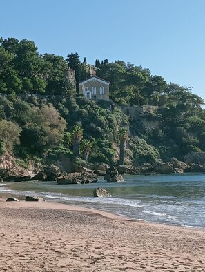 Un paisaje costero con un edificio en una ladera, con vista a una playa.
