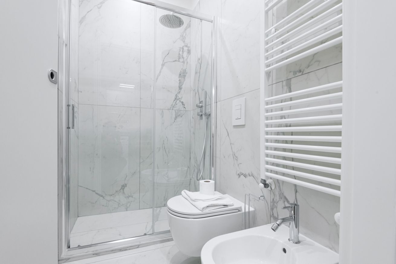 Un baño moderno con ducha de vidrio, inodoro blanco y lavamanos con espejo.