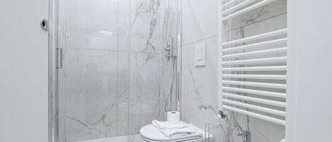 Un baño moderno con ducha de vidrio, inodoro blanco y lavamanos con espejo.