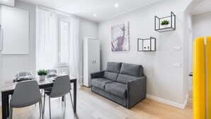 A modern living room with a grey sofa, a dining table with chairs, and a kitchen area. - Easylife -Modern and elegant in the heart of Milan (Milano)
