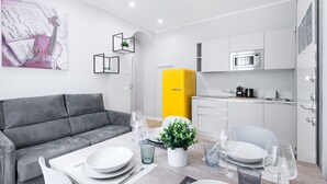A modern living room with a grey sofa, dining table set with plates and glasses, a yellow cabinet, and a kitchen area with a microwave. - Easylife -Modern and elegant in the heart of Milan (Milano)