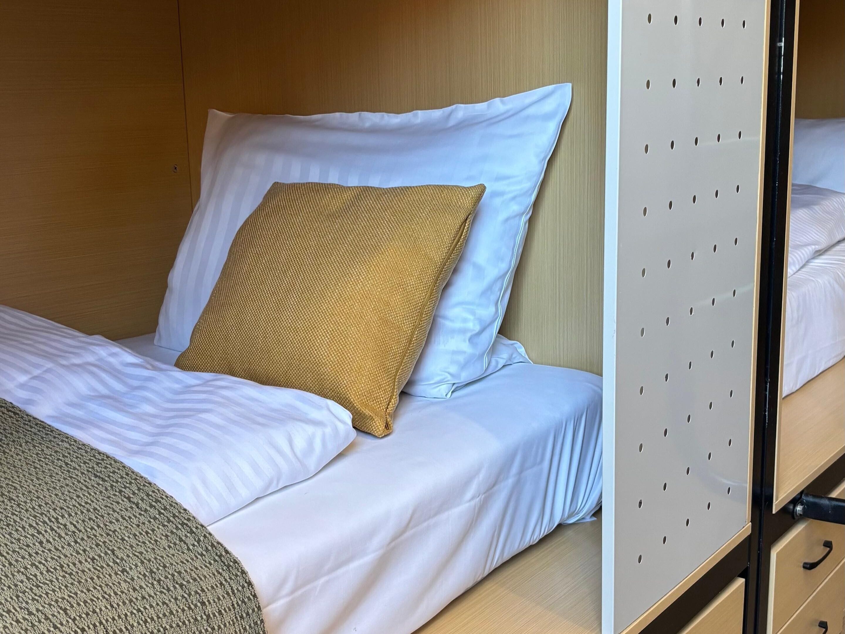 Un lit superposé avec une literie blanche et un coussin marron tissé.
