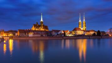A historic building with two prominent towers, a bridge, and a calm river reflecting the structure.