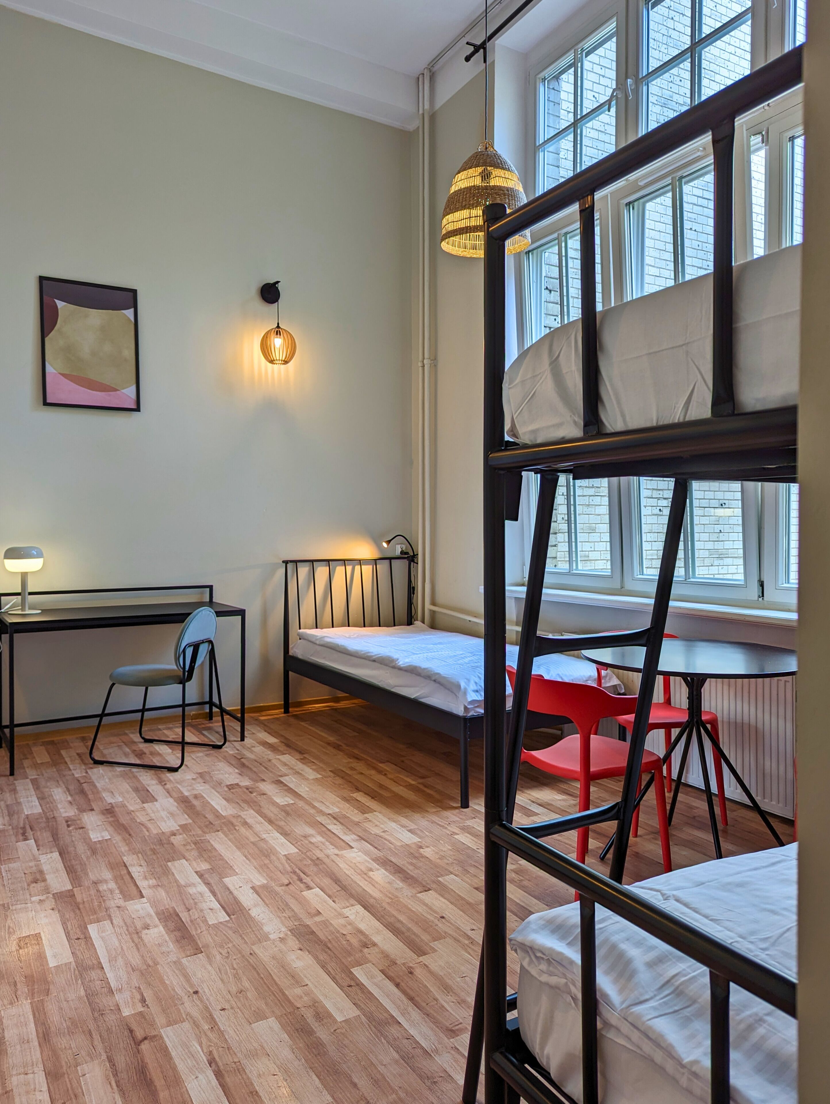 A dormitory room with bunk beds, a desk, a chair, and a radiator.
