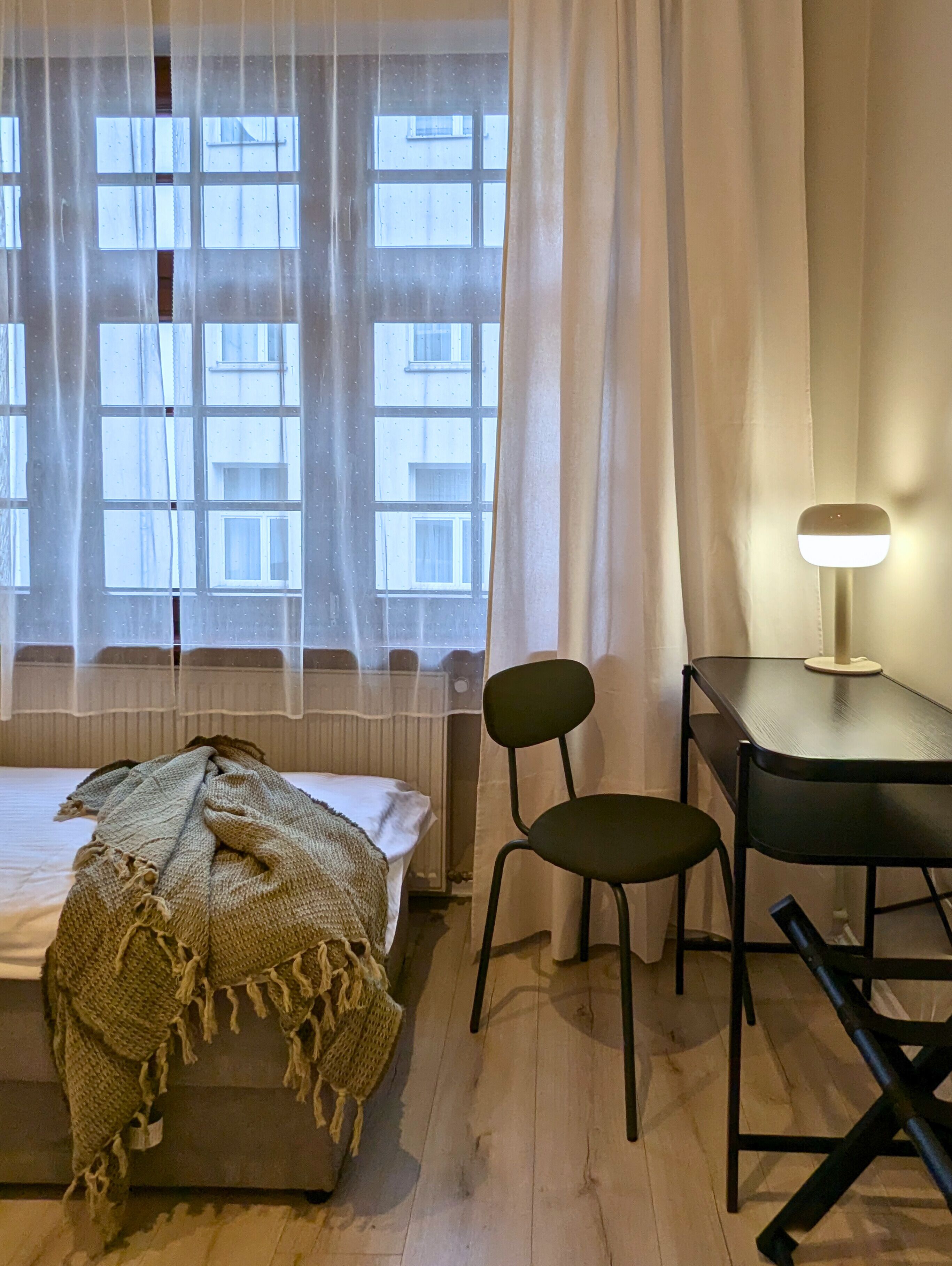 A bedroom with a bed, a desk, two chairs, and a lamp.