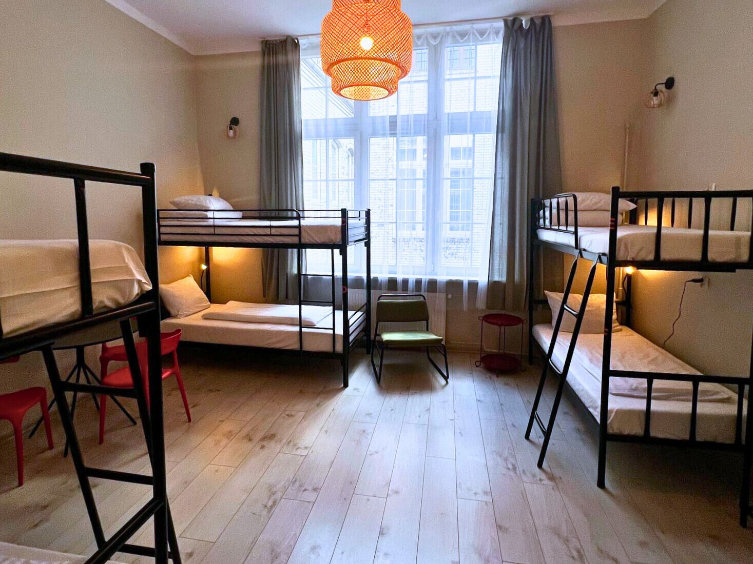 Habitación tipo dormitorio con literas, una silla pequeña, un taburete rojo y una lámpara colgante.