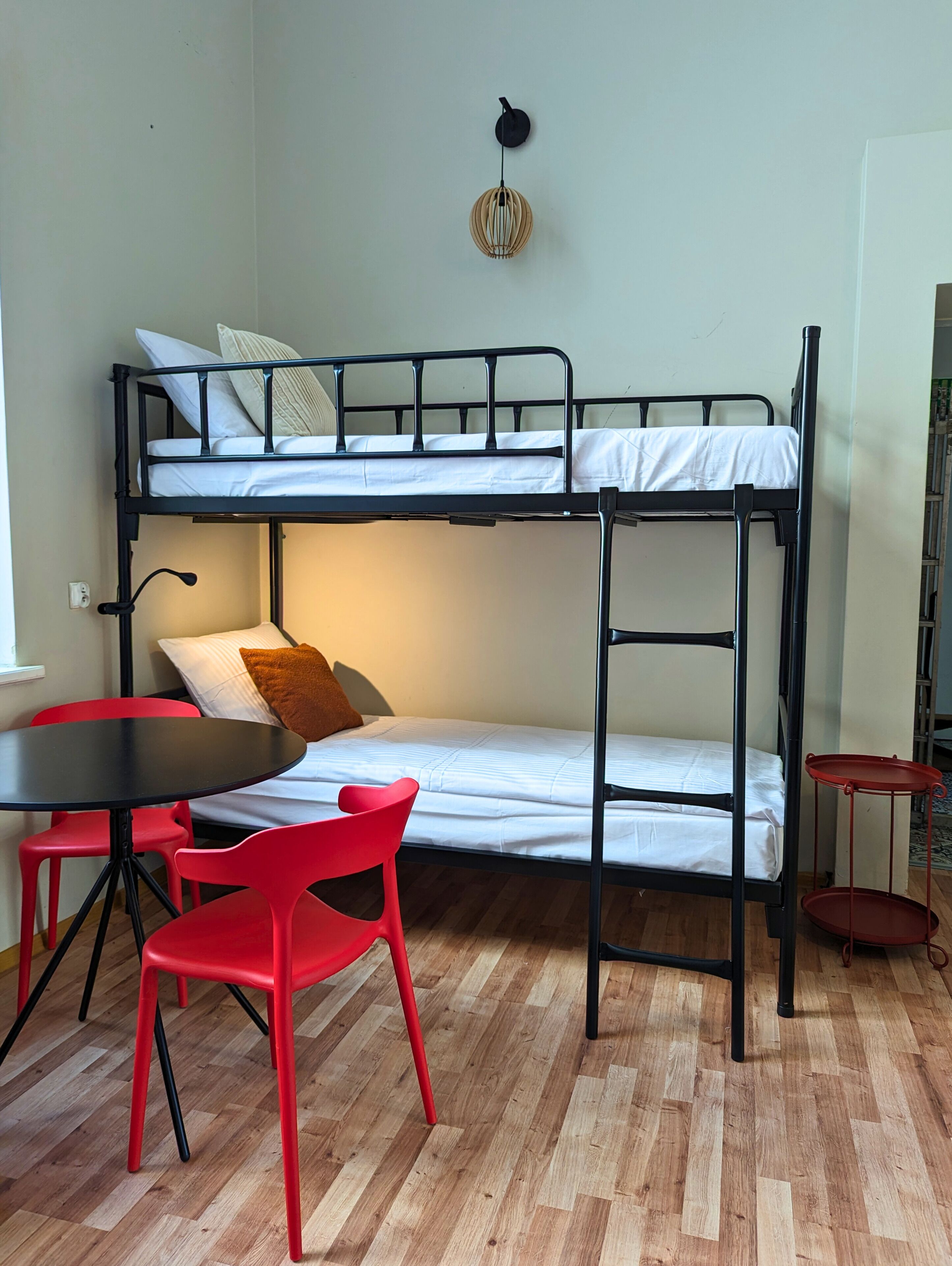 A bunk bed with a table and chairs, a hanging light fixture, and a small red table.