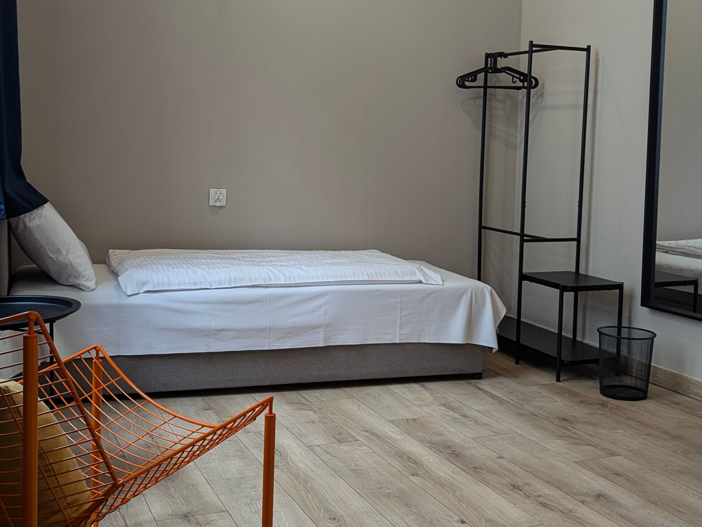 A bedroom with a bed, a chair, a tall black shelf, and a mirror.