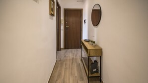 Un couloir avec une porte en bois, une console surmontée d’un miroir et une petite étagère.