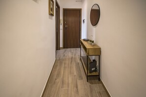 A hallway with a wooden door, a console table with a mirror, and a small shelf.