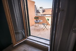 Ein Balkon mit Tisch und Stühlen, Blick auf Gebäude, und eine Tür, die auf den Balkon führt.