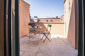 A balcony with a table and chairs, a small plant, and a view of buildings in the background.