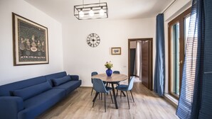 Un salon moderne avec un canapé bleu, une table à manger en bois avec des chaises, une horloge et un tableau encadré accroché au mur.