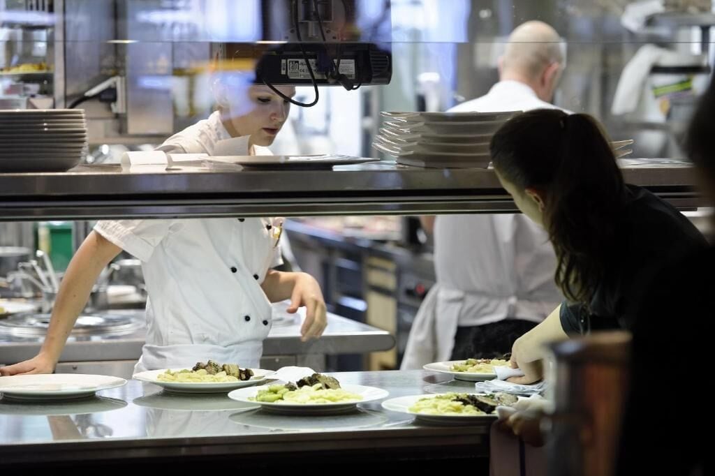 Una cocina con chefs preparando alimentos, mostradores de acero inoxidable y una zona de exhibición de comida.
