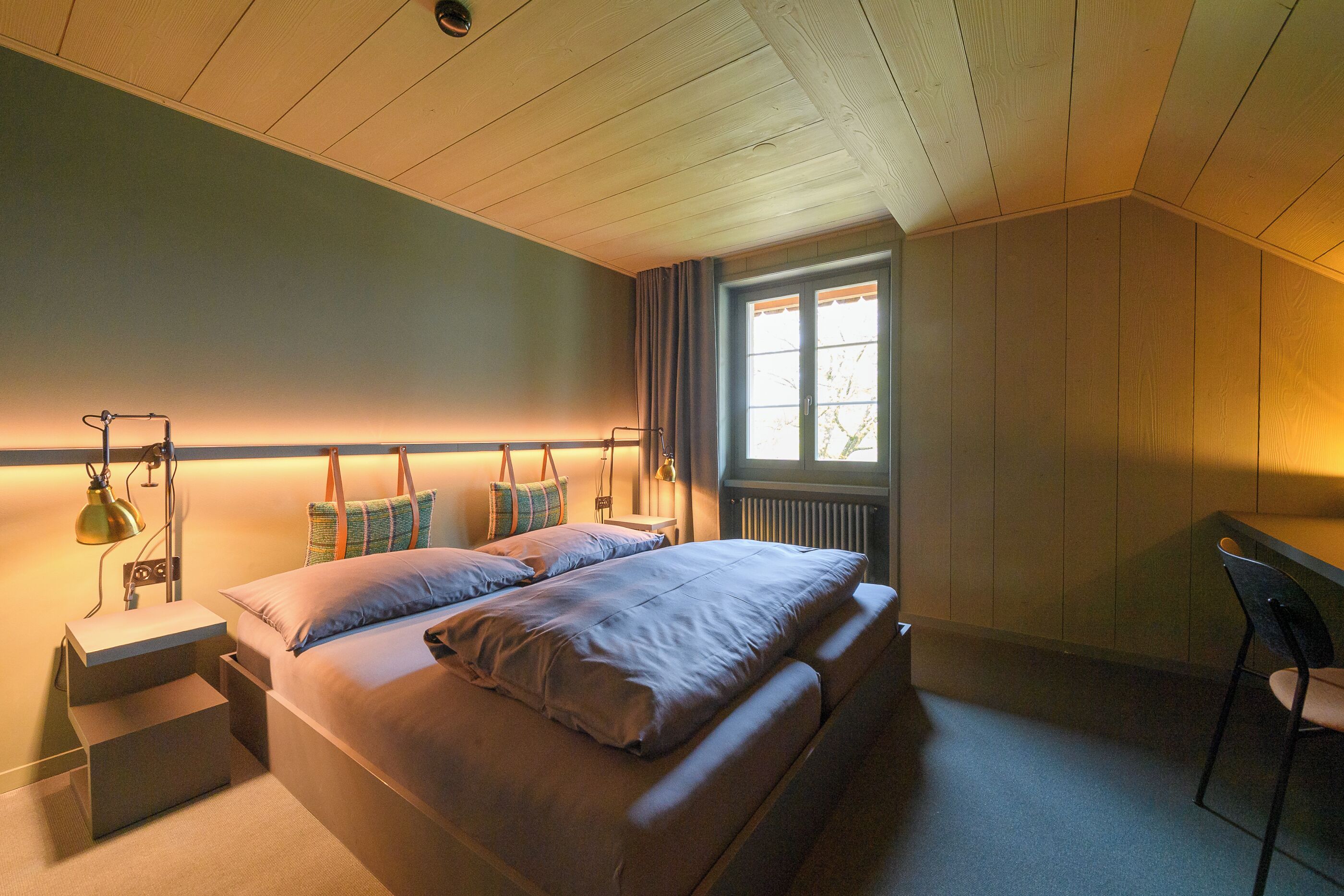 A bedroom with a bed, bedside tables, a desk, and a window.