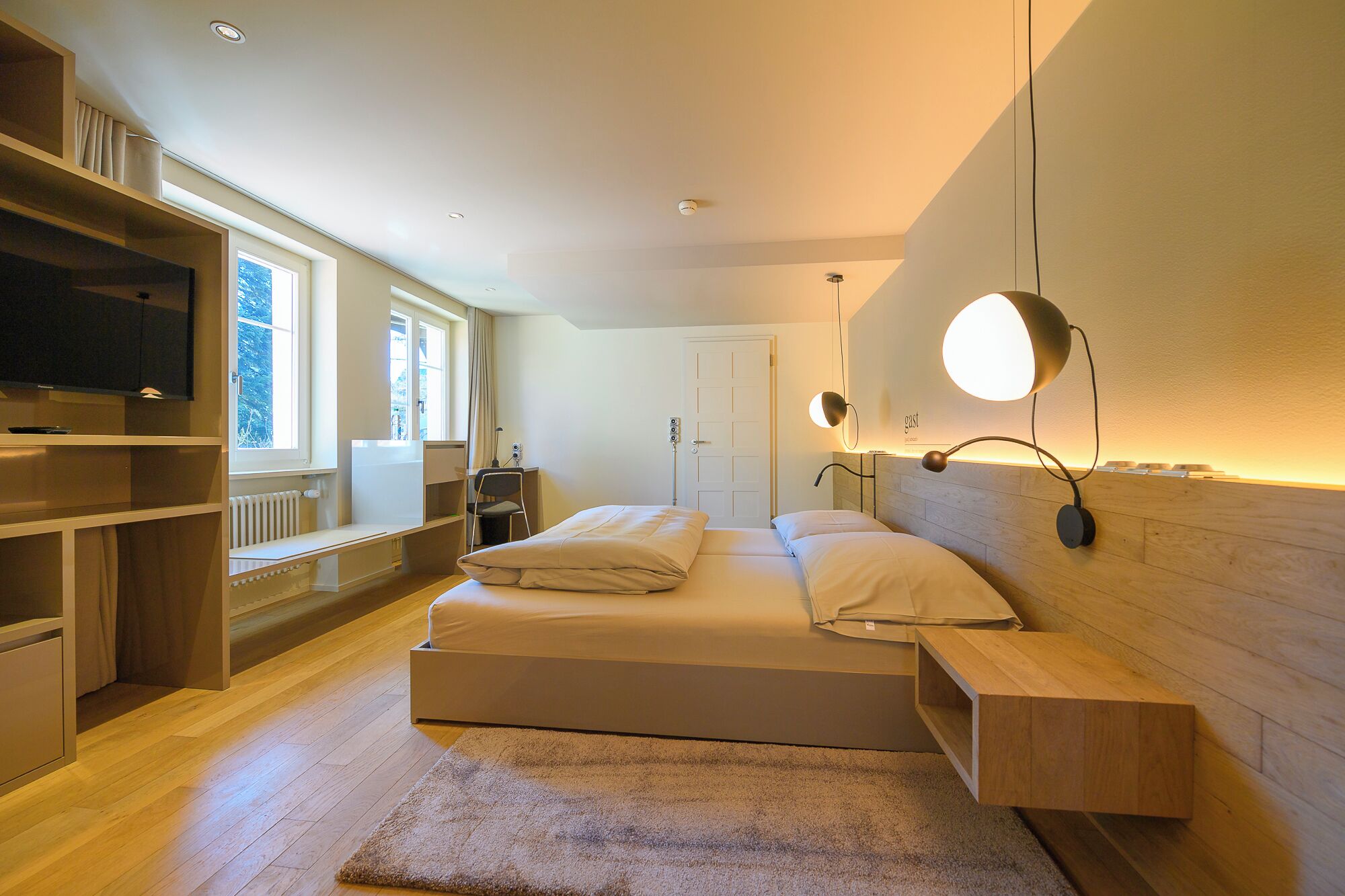 A modern bedroom with a large bed, built-in shelving, a TV, and a desk.