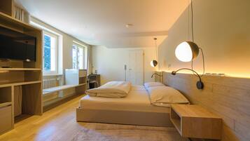 A modern bedroom with a large bed, built-in shelving, a TV, and a desk.