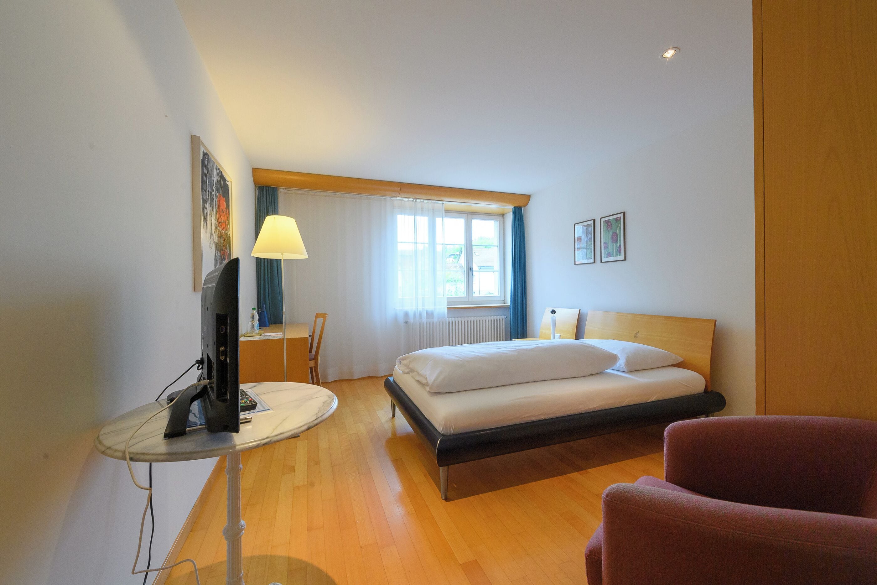 Ein Hotelzimmer mit einem Bett, einem Schreibtisch mit Computer, einem Sessel und einer Lampe.