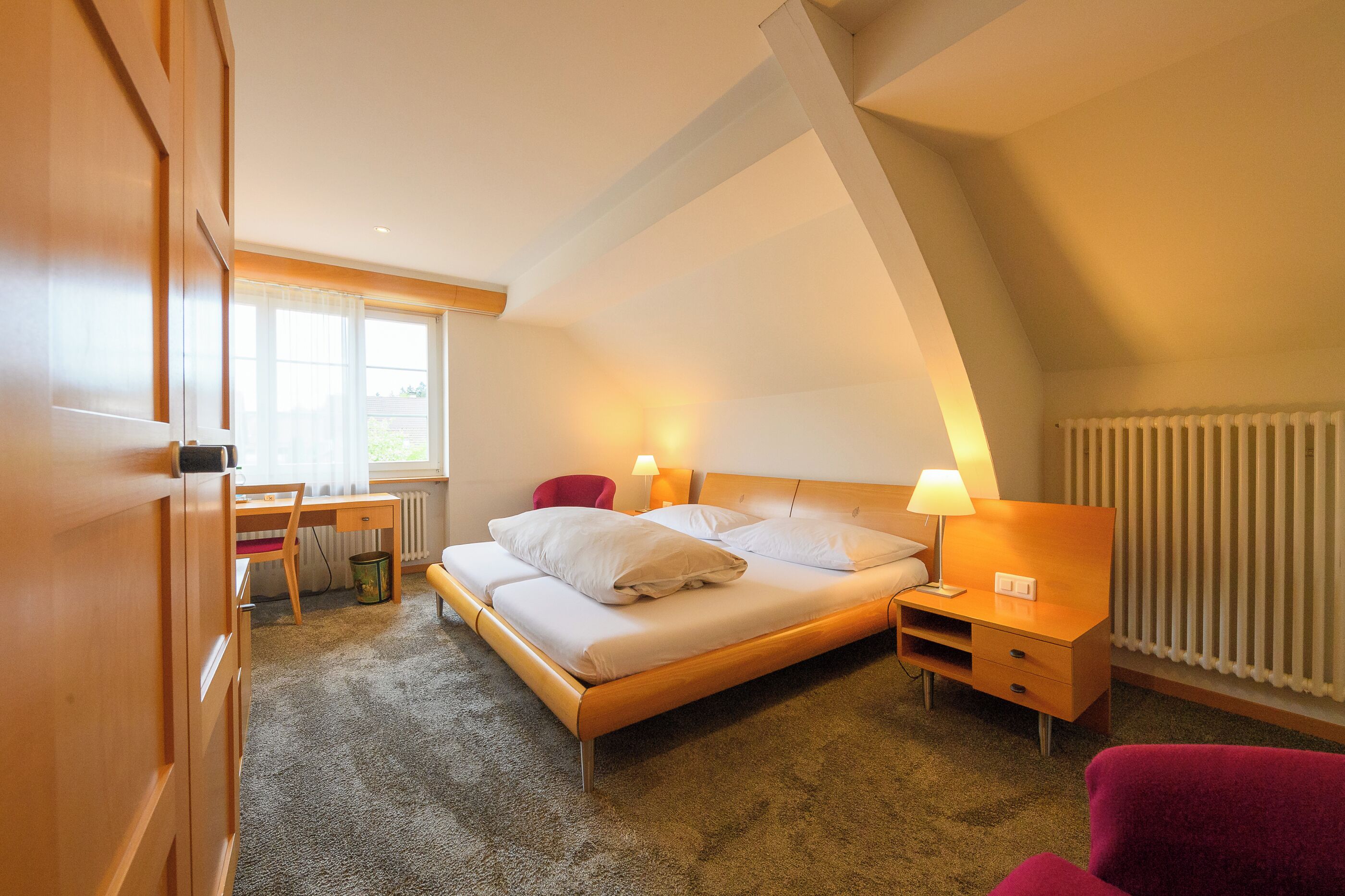 A bedroom with a bed, bedside tables, a desk, and a chair.