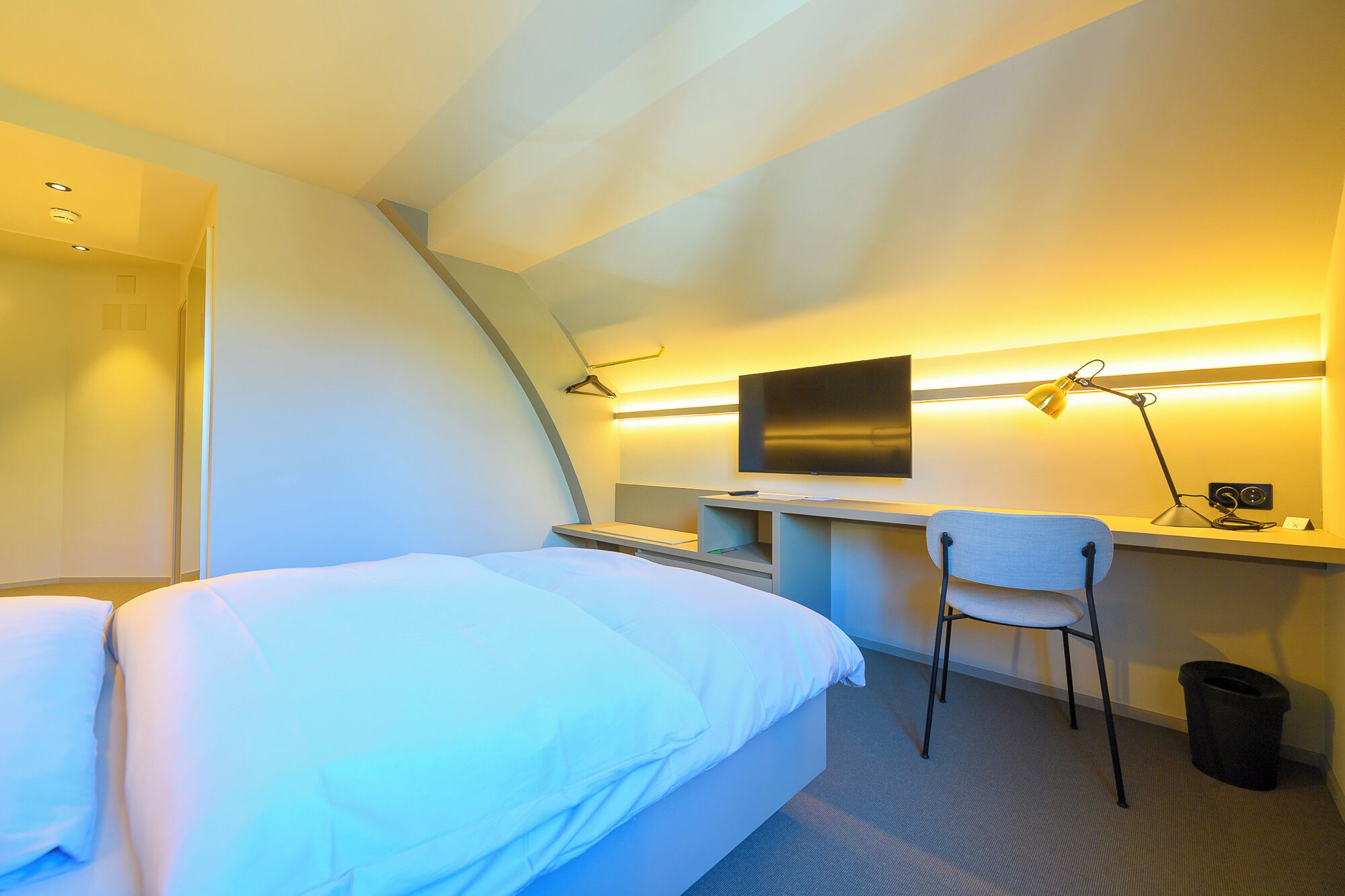 Une chambre d’hôtel équipée d’un lit, d’un bureau, d’une chaise, d’une télévision et d’une poubelle.