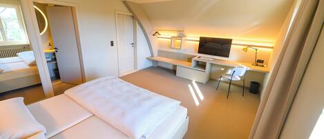 Una habitación de hotel moderna con una cama grande, un escritorio con una silla, televisión y un baño con espejo e inodoro.