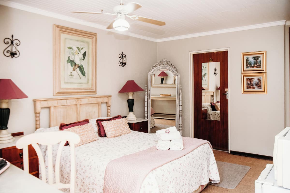 Ein Schlafzimmer mit Bett, Nachttischlampen, Deckenventilator, Spiegel und gerahmten Bildern an der Wand.