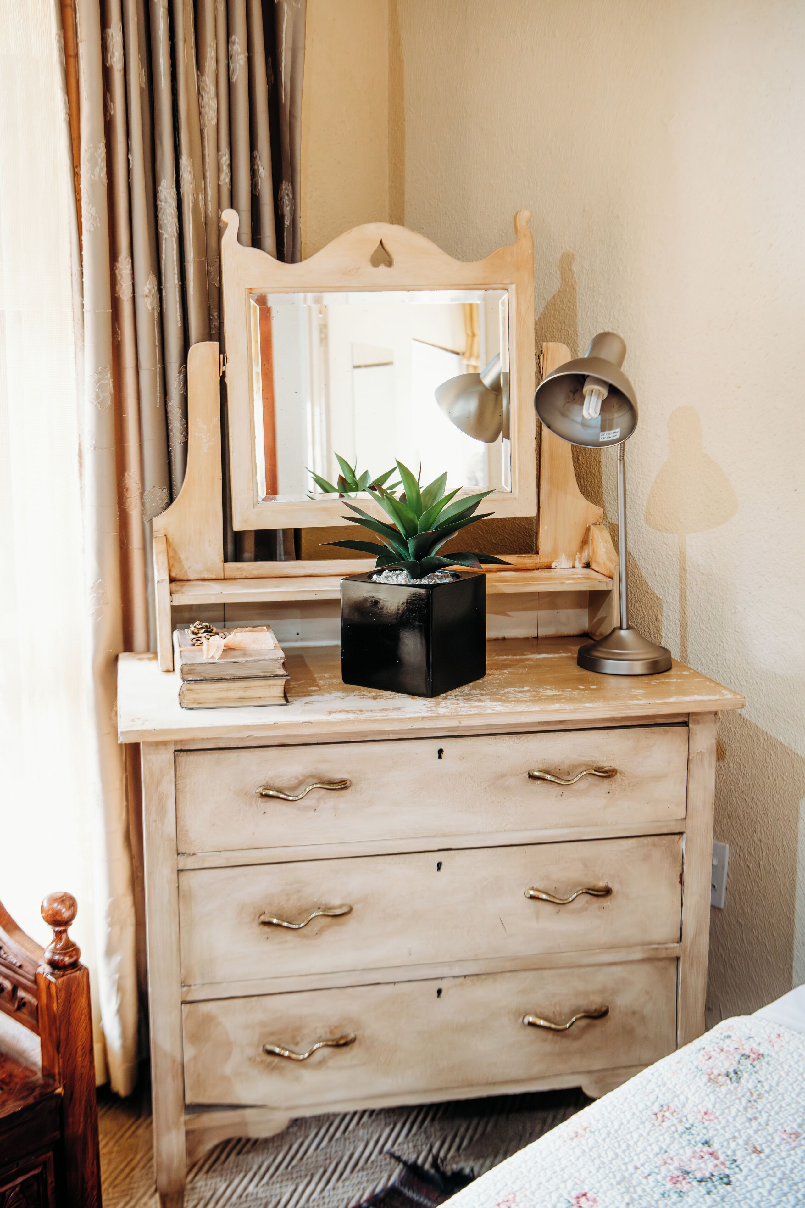 A wooden dresser with a mirror, a lamp, and a potted plant.