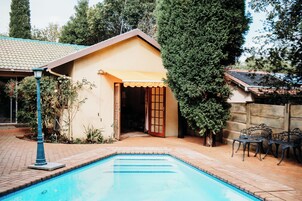 Una piscina con solárium de baldosas, un porche cubierto y mobiliario exterior.