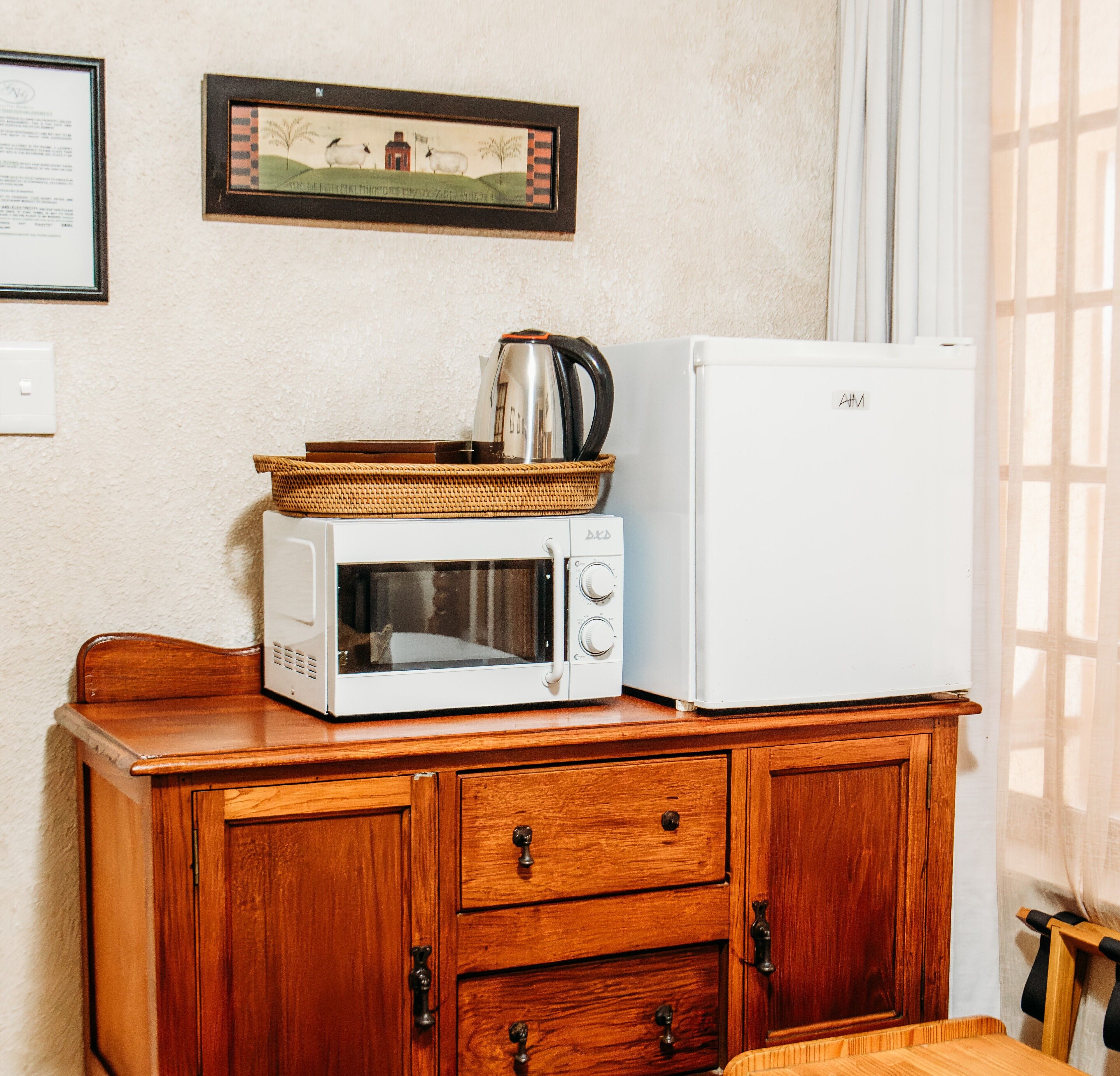 A kitchenette with a microwave, toaster, and kettle on a wooden cabinet.