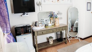Ein Schlafzimmer mit Fernseher, Kommode, Spiegel und einer kleinen Küchenzeile.