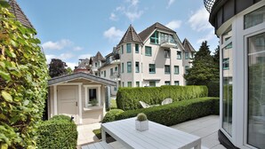 Un immeuble résidentiel moderne doté d’un jardin bien entretenu, d’une table extérieure blanche et d’un petit abri de jardin.