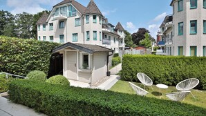 Un immeuble d’appartements moderne doté de nombreux balcons et d’un petit espace jardin avec des chaises blanches.