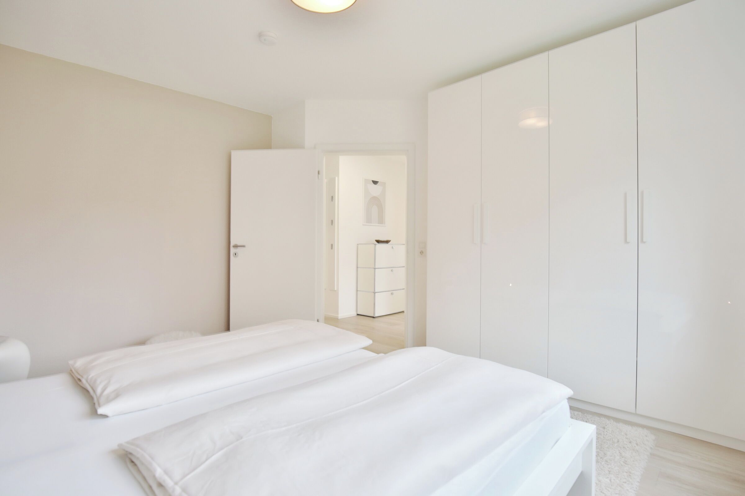 A modern, minimalist bedroom with a large wardrobe, a neatly made bed, and a clean, bright atmosphere.