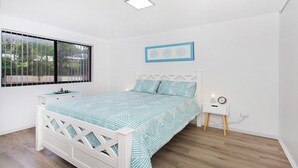 A bedroom with a bed, a nightstand, a wall clock, and a window with blinds. - My Coastal Getaway - Kiama (Kiama)