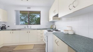 A modern kitchen with white cabinets, a stove, and a window. - My Coastal Getaway - Kiama (Kiama)