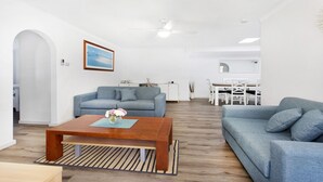 A modern living room with a grey sofa, a wooden coffee table, and a dining area with a white table and chairs. - My Coastal Getaway - Kiama (Kiama)