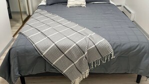 Ein Bett mit grauer Steudecke, zwei Kissen und einer Streifen-Decke.
