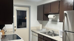 Eine moderne Küche mit dunklen Schränken, einem Edelstahlkühlschrank, einem eingebauten Backofen und einem Fenster mit Aussicht.