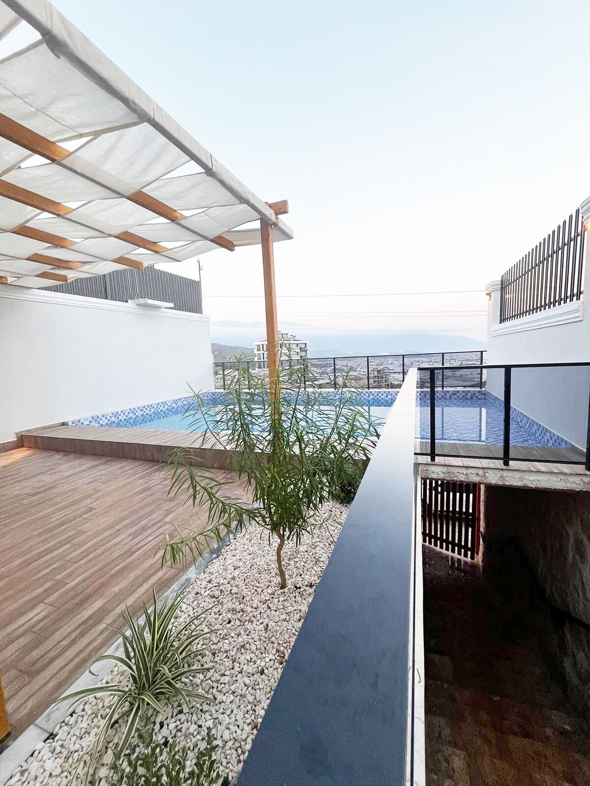 A rooftop terrace with a pool, wooden deck, and a view of the cityscape.