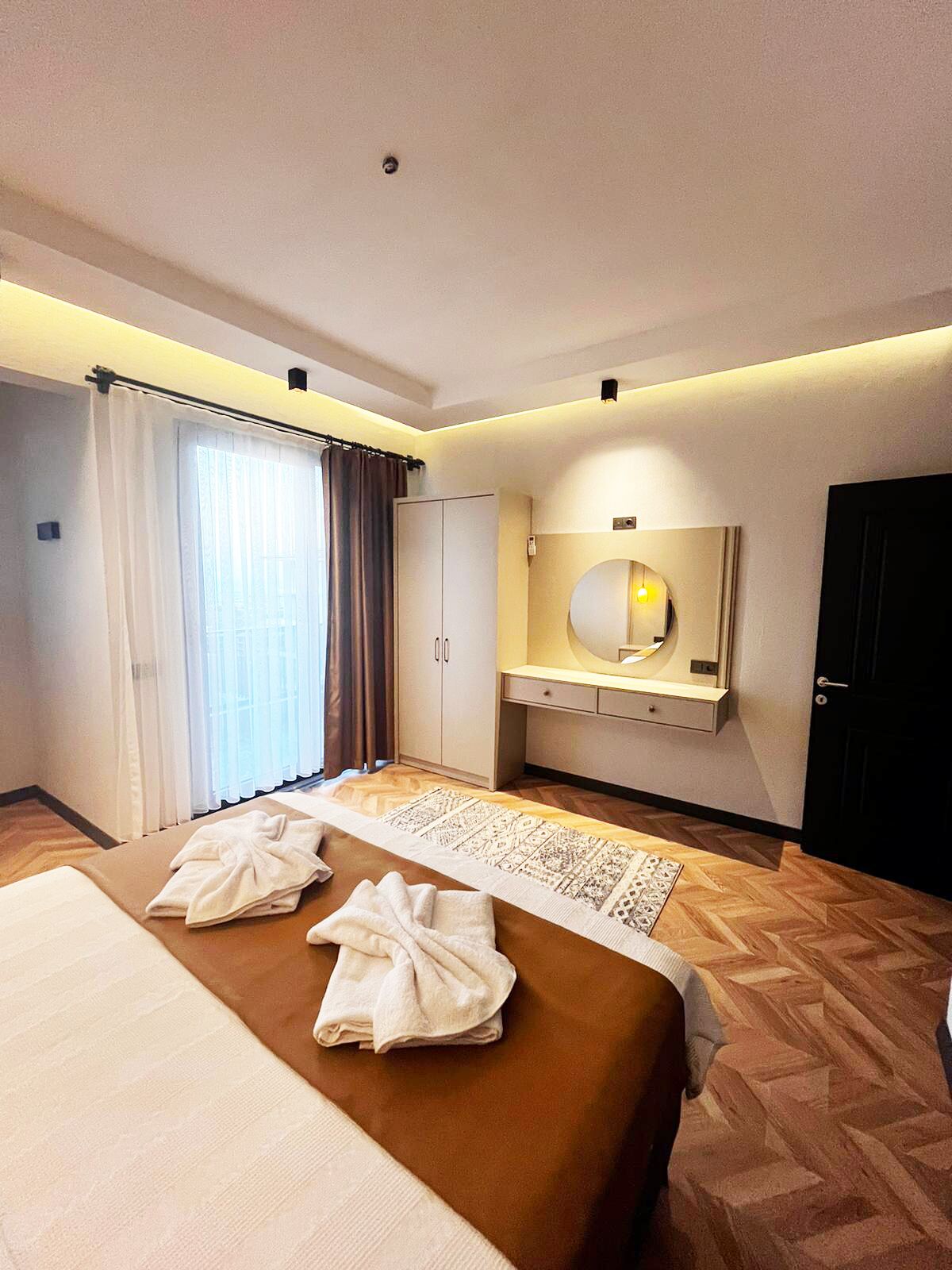 A hotel room with a bed, a bedside table, a mirror, a wardrobe, and a window with curtains.