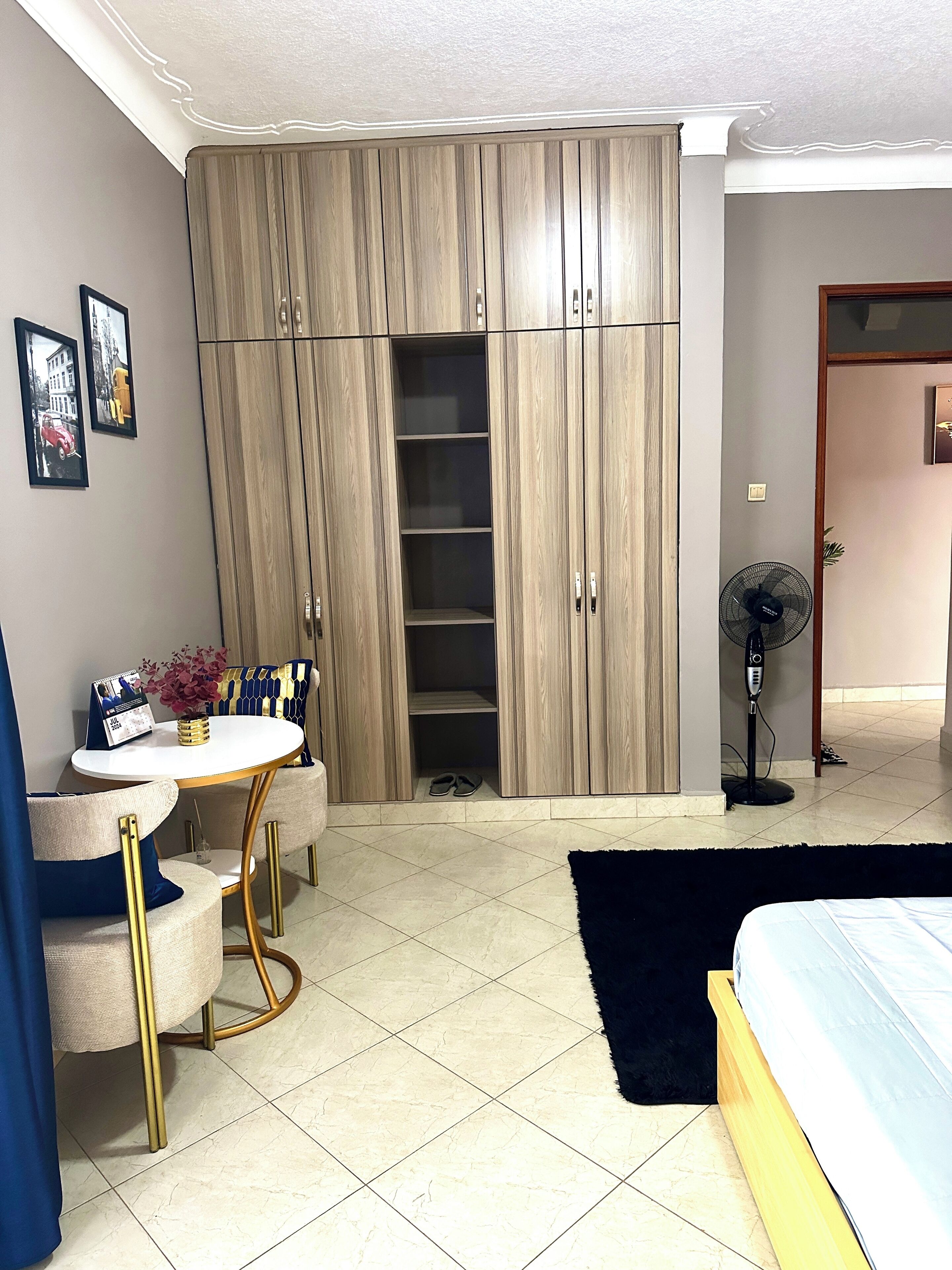 A bedroom with a bed, a wardrobe, a small table with a vase, and a chair.